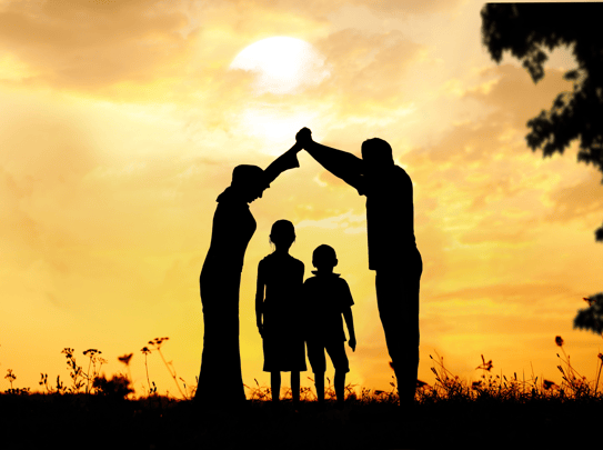 A family silhouetted by the sunset with the parents creating a roof over the children with their arms