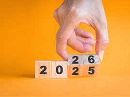 A hand flipping wooden blocks with numbers from 2025 and 2026