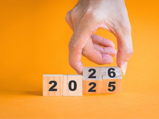A hand flipping wooden blocks with numbers from 2025 and 2026