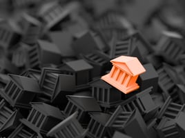 Orange figurine of a bank on top of a pile of black bank figurines