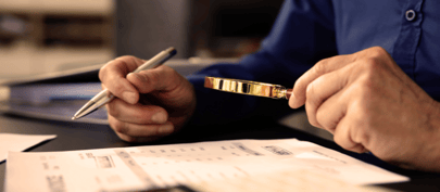 Document on desk and male hands, one holding a pen and other magnifying glass