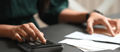 Image shows a person using a calculator at a desk with papers in front of them