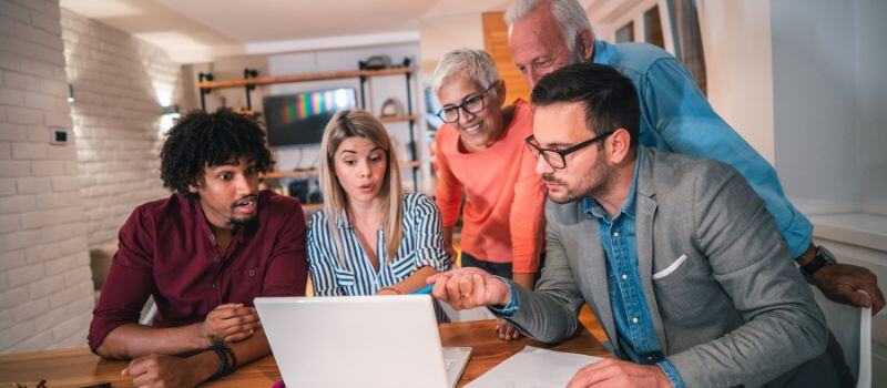 Multi generational and racial family gathered around a laptop on tablet with a man in suit explaining something