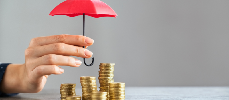 Hand holding an umbrella above coins