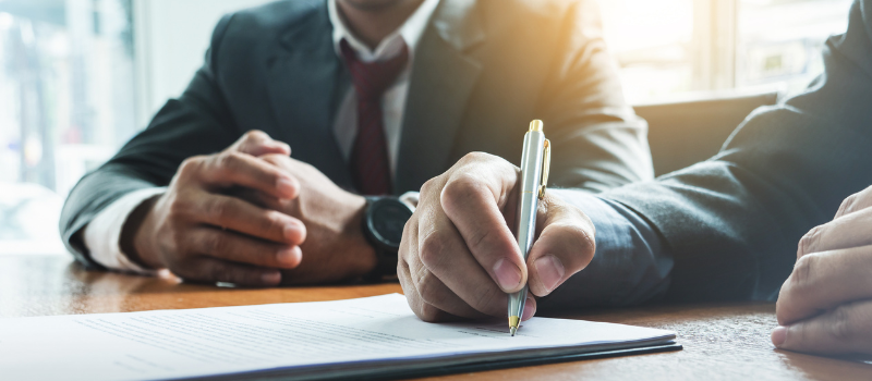 man signing paper with a person in a suit watching