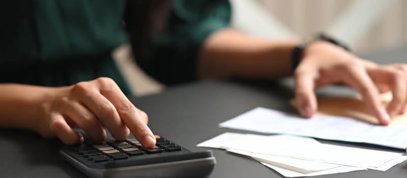 Image shows a person using a calculator at a desk with papers in front of them