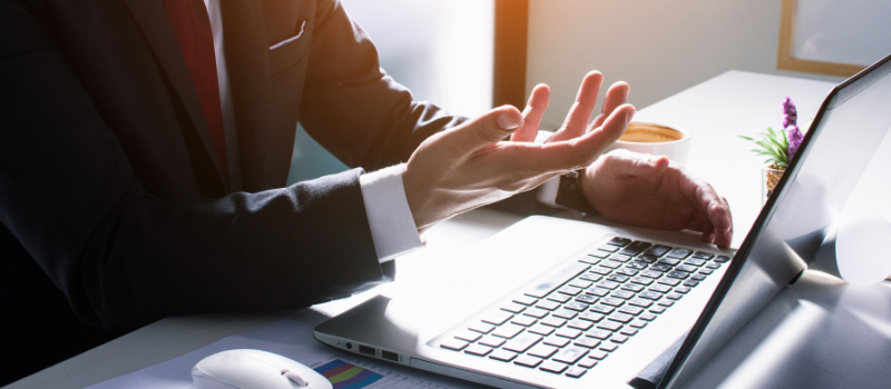 Man in suit gesturing with hands during video meeting on a laptop.