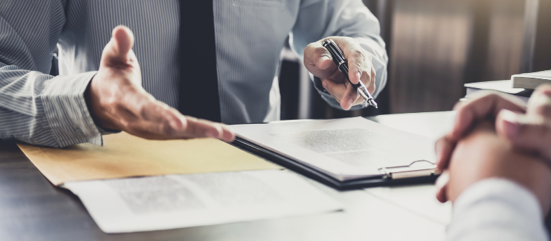 Business man at desk with forms, talking to another person.