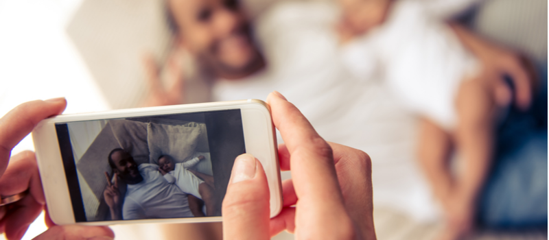 Woman taking a photo of a man and baby using her phone